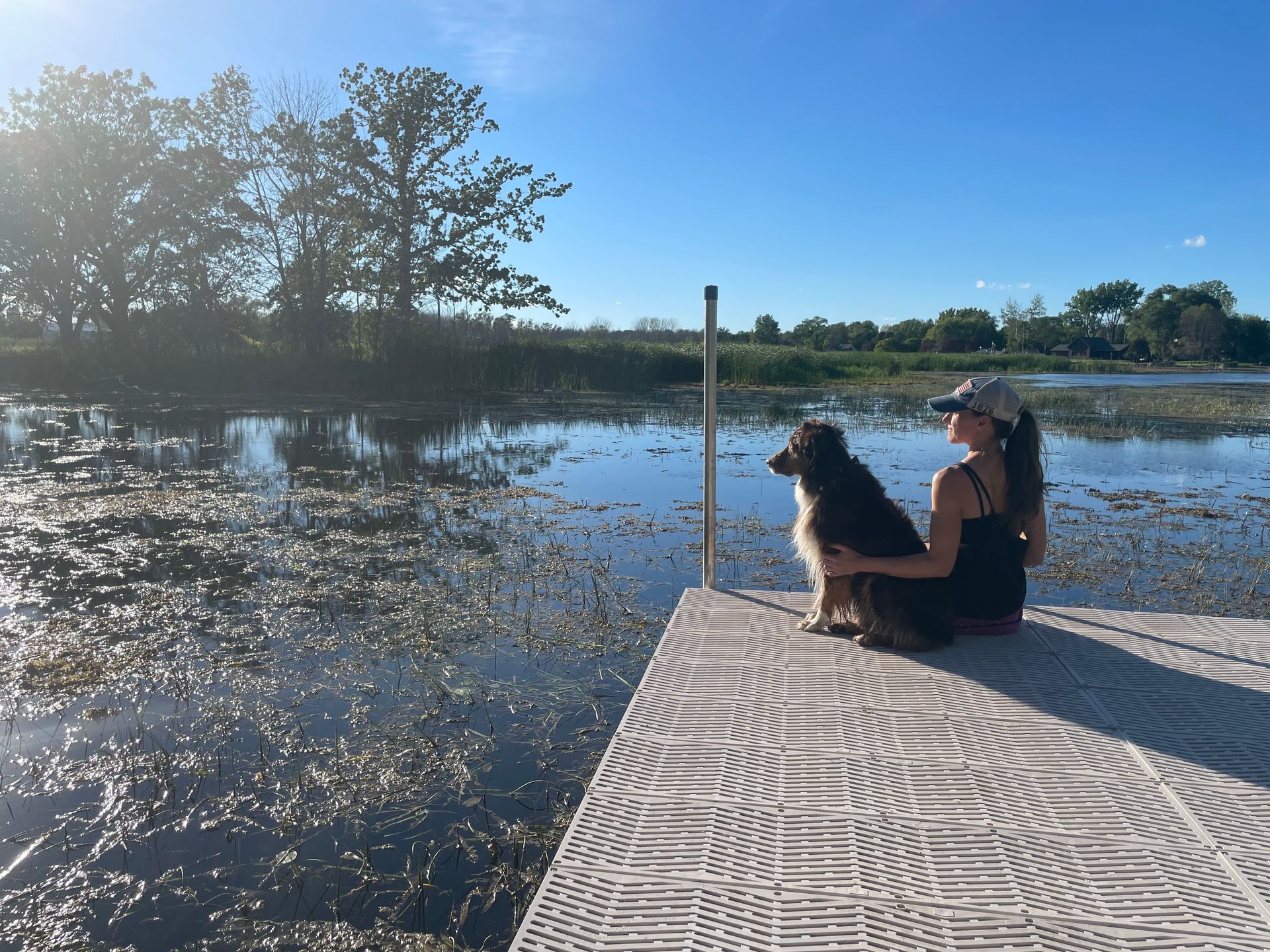 A dog trainer is sitting on a dock with a dog.