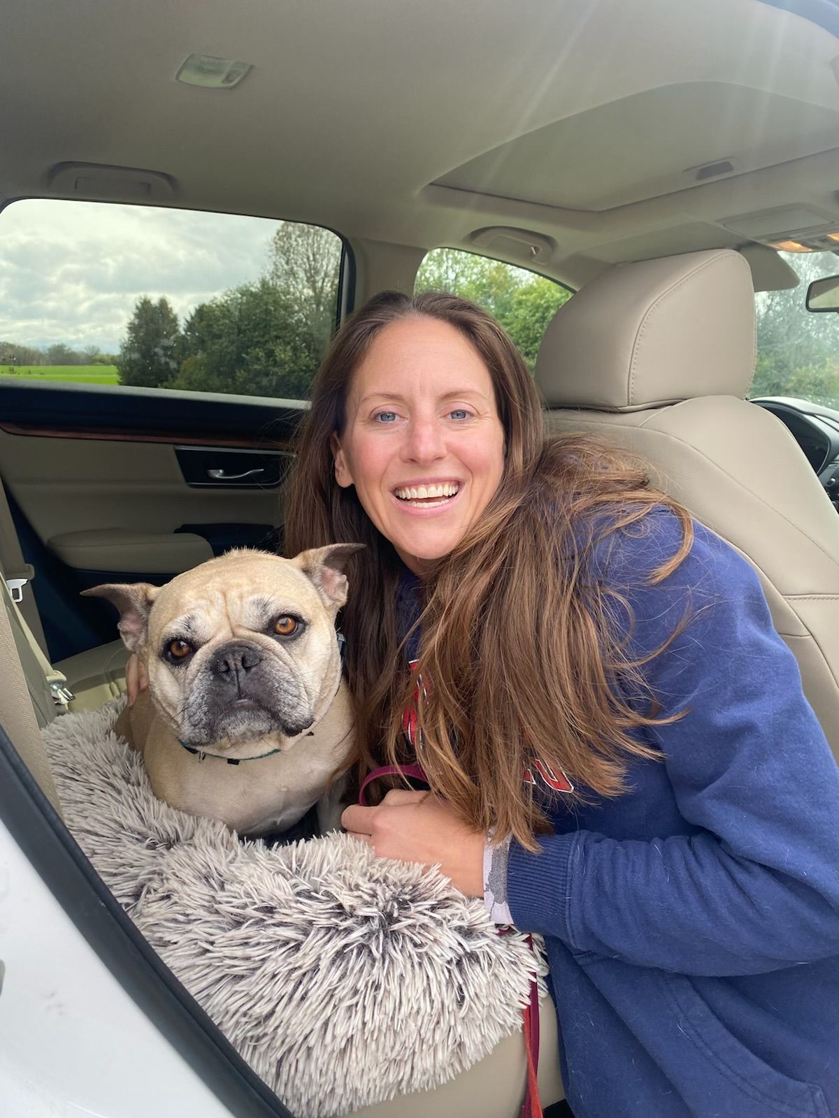 A dog trainer is sitting in the back seat of a car with a dog.