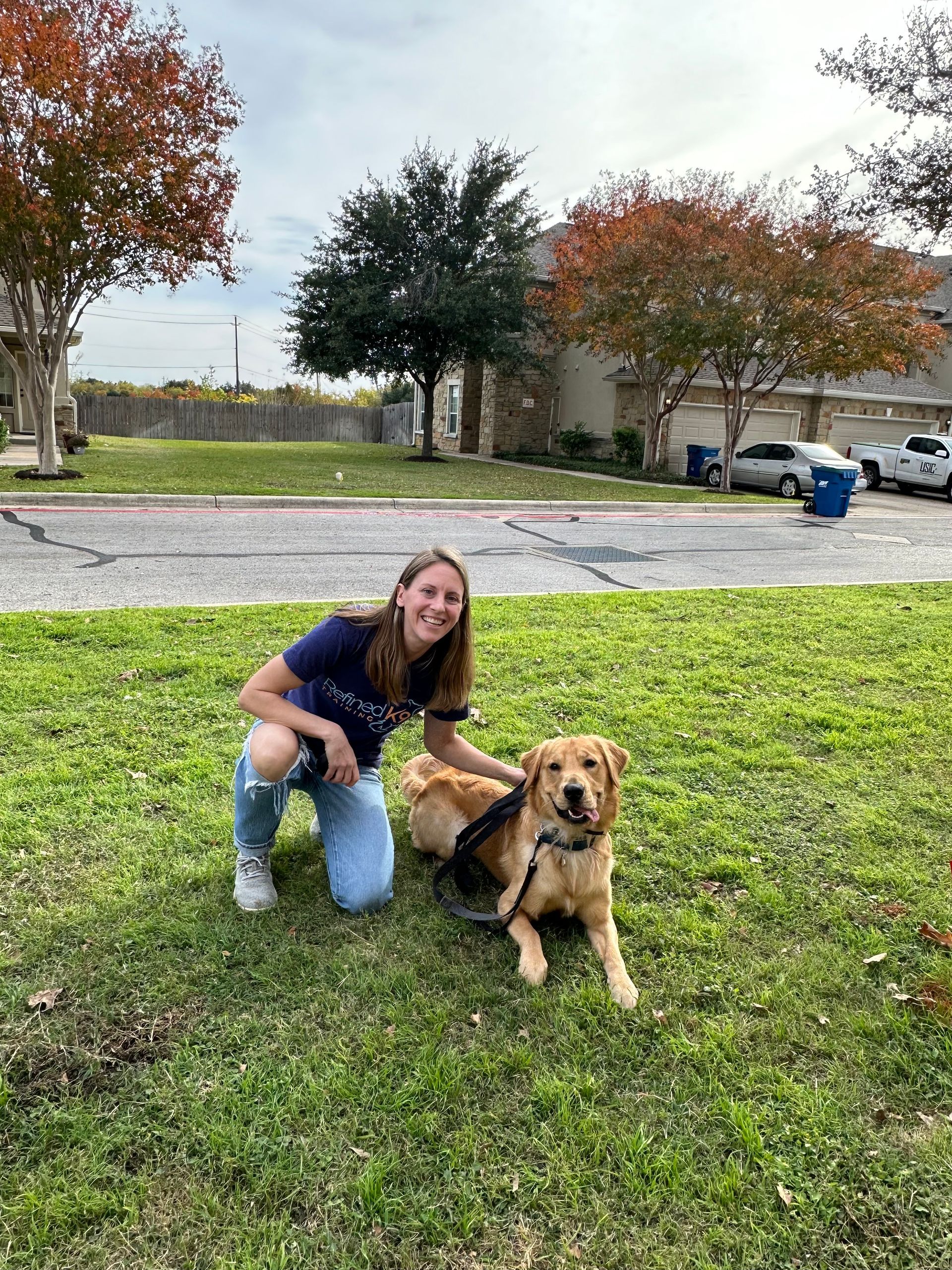 A woman is kneeling down next to a dog in the grass.