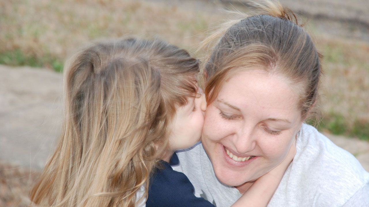 A little girl is whispering into a woman 's ear.