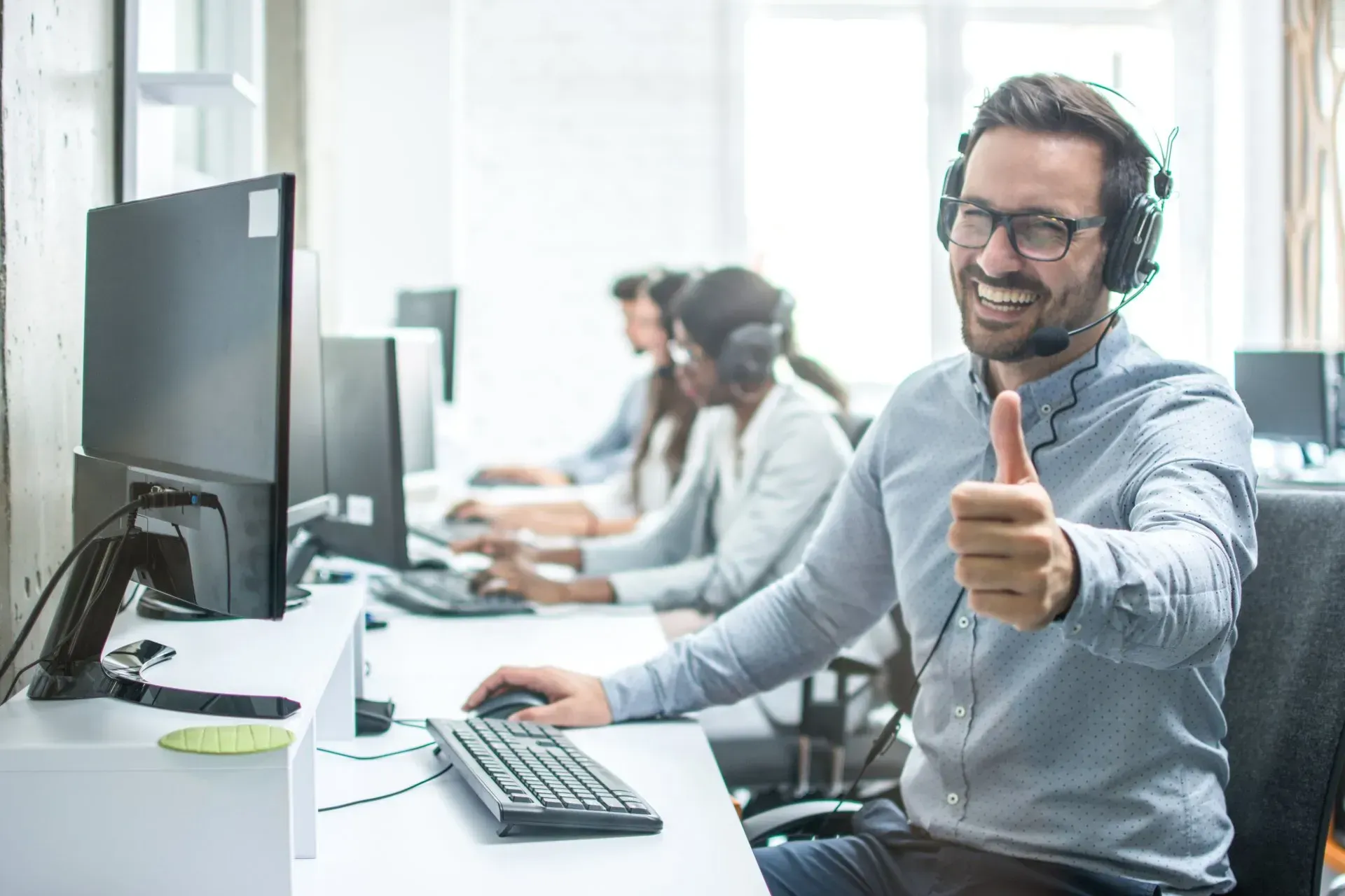 A man wearing a headset is giving a thumbs up in a call center.