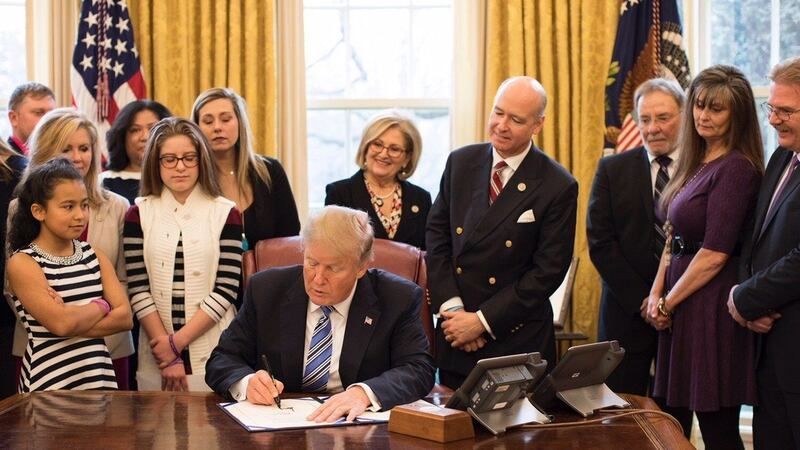 A man in a suit and tie is signing a document in front of a group of people.