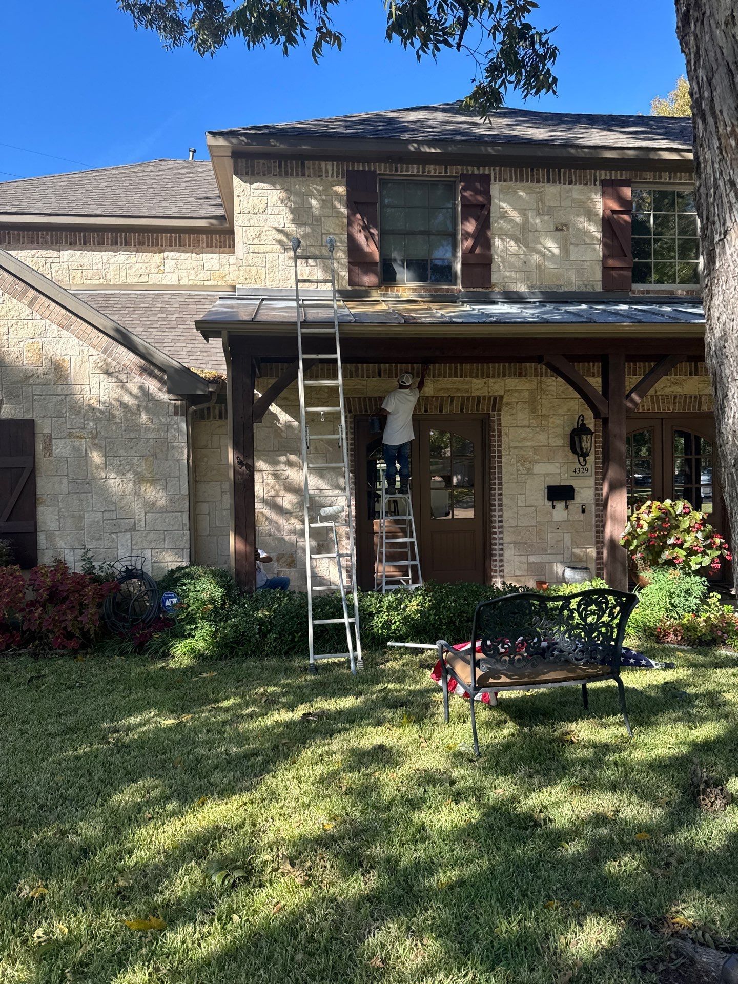 A person digs a trench in a backyard near a small excavator, a tree, and a house.