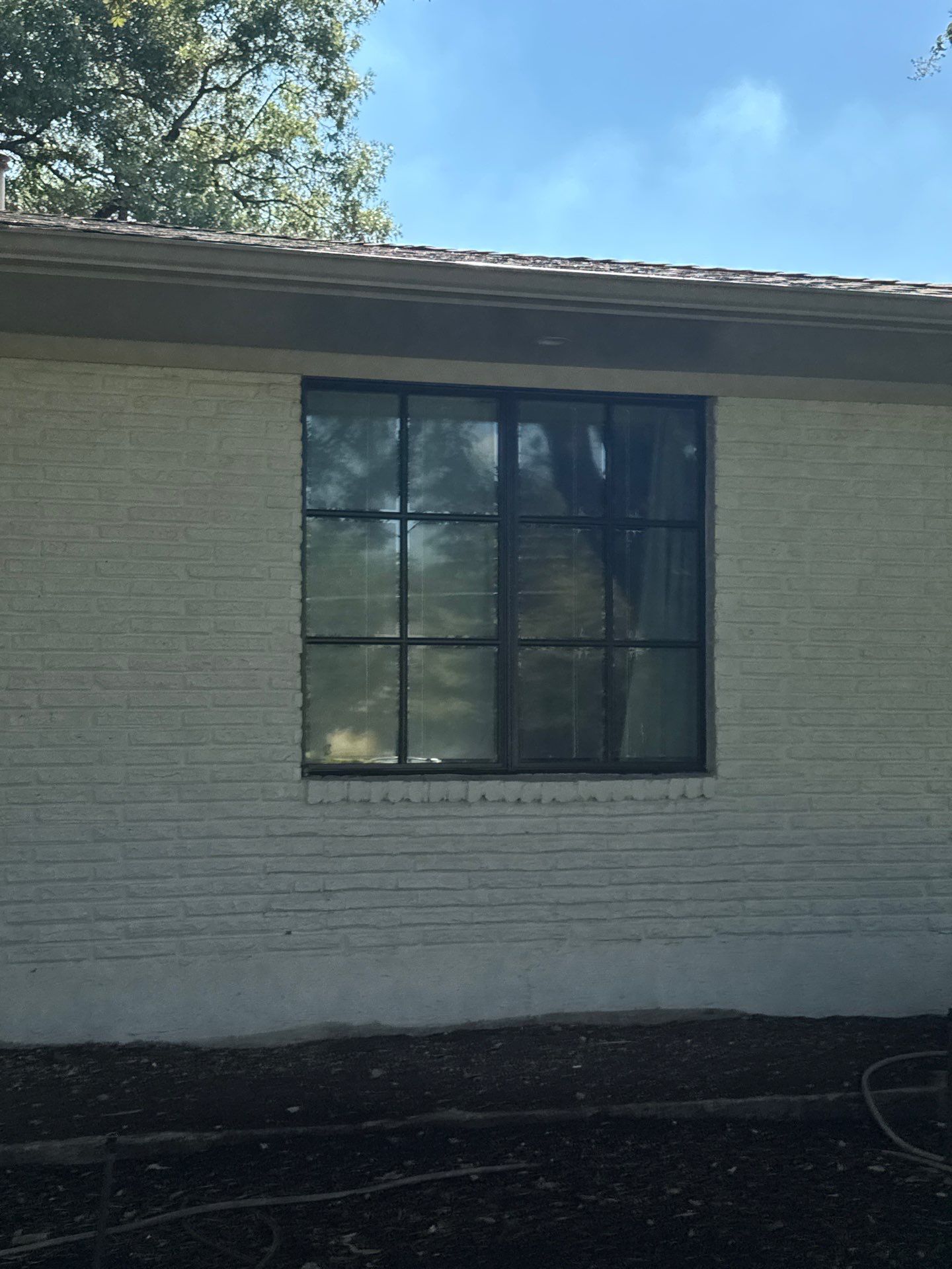 A person digs a trench in a backyard near a small excavator, a tree, and a house.