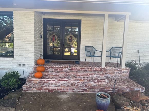 Front porch with brick steps, double glass doors, pumpkins, and two metal chairs on a white house