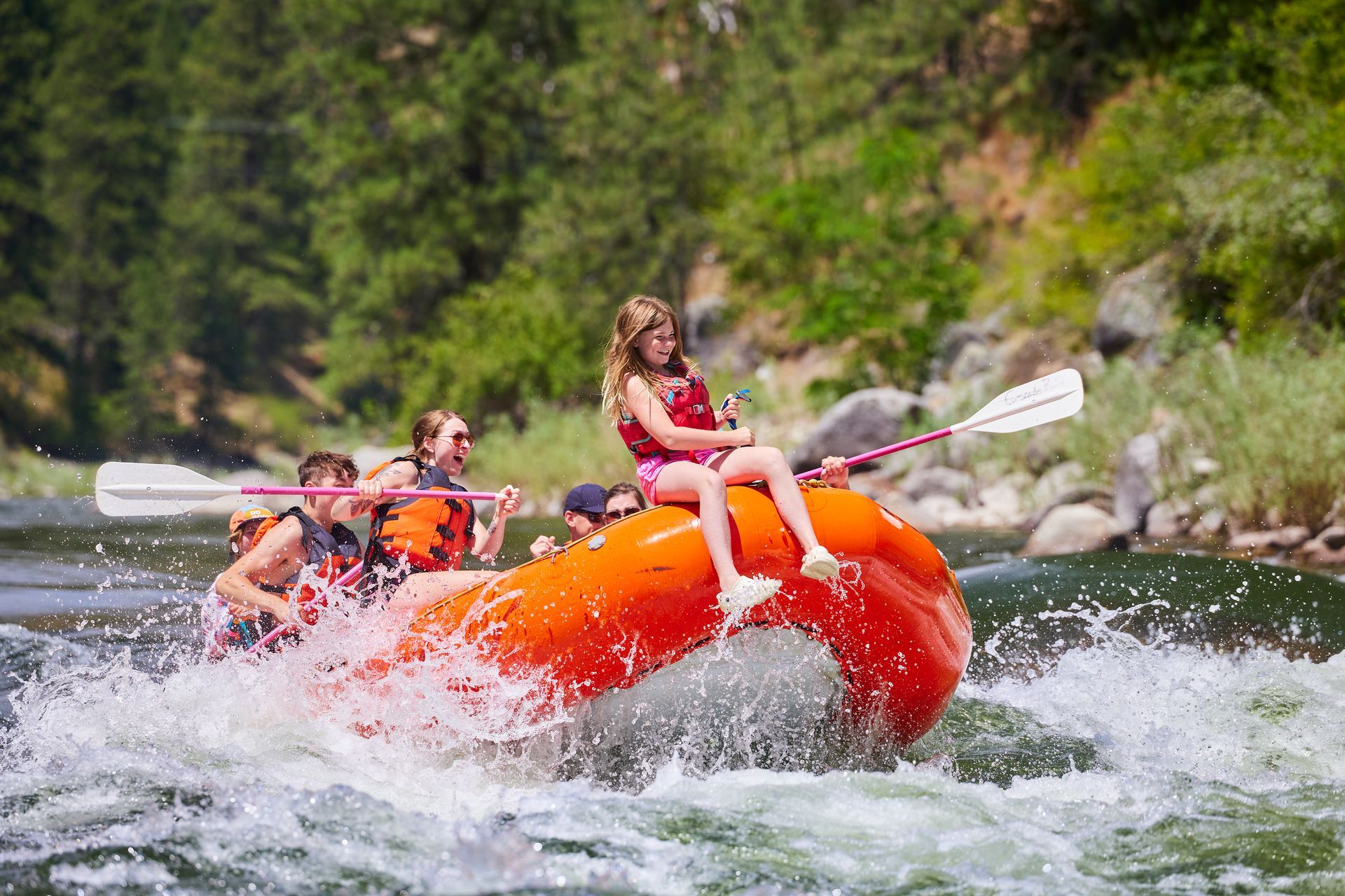 child riding the front of a raft through whitewater rapids