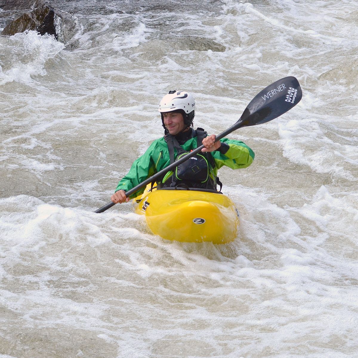 Yellow whitewater kayaker in rapid with smile,