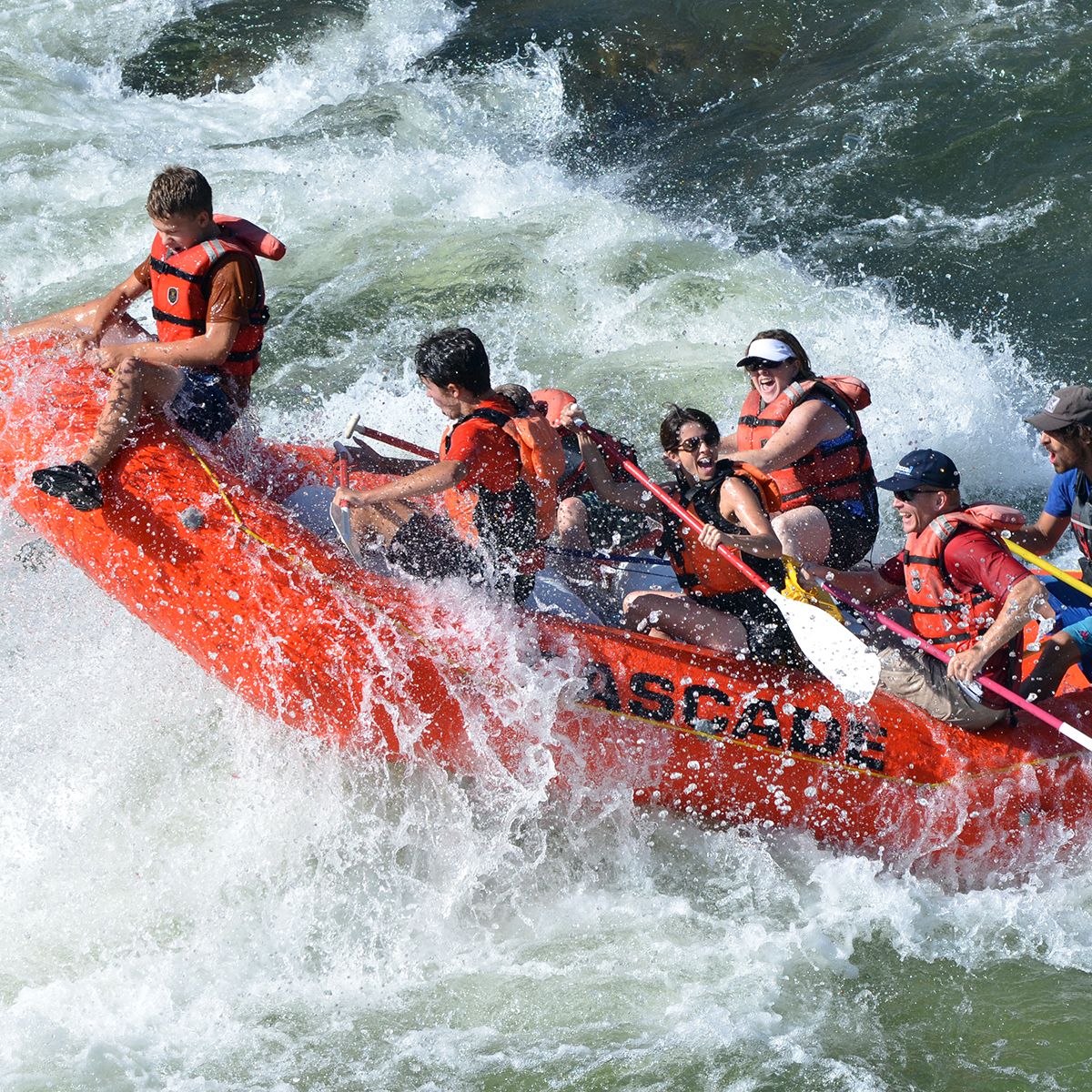 Orange whitewater raft with families smiling in rapid.