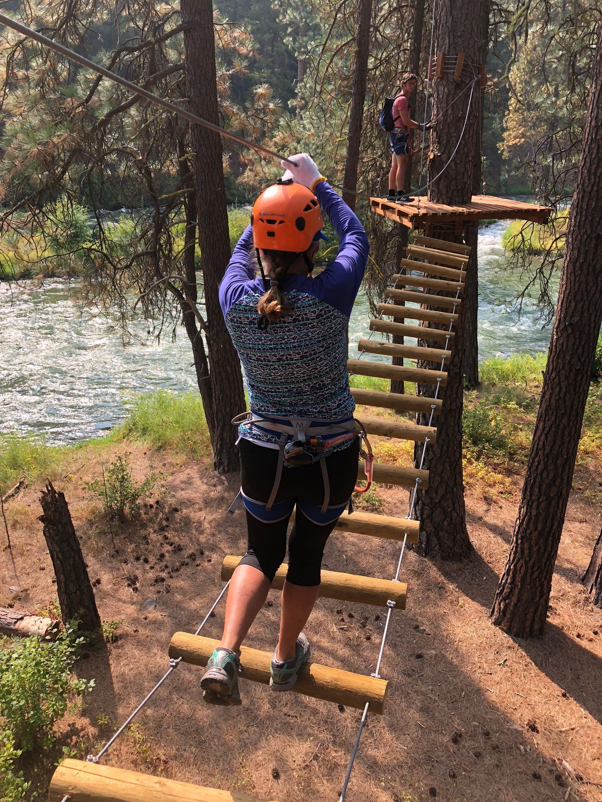 Woman crossing obstacle in high ropes challenge course with river in the background