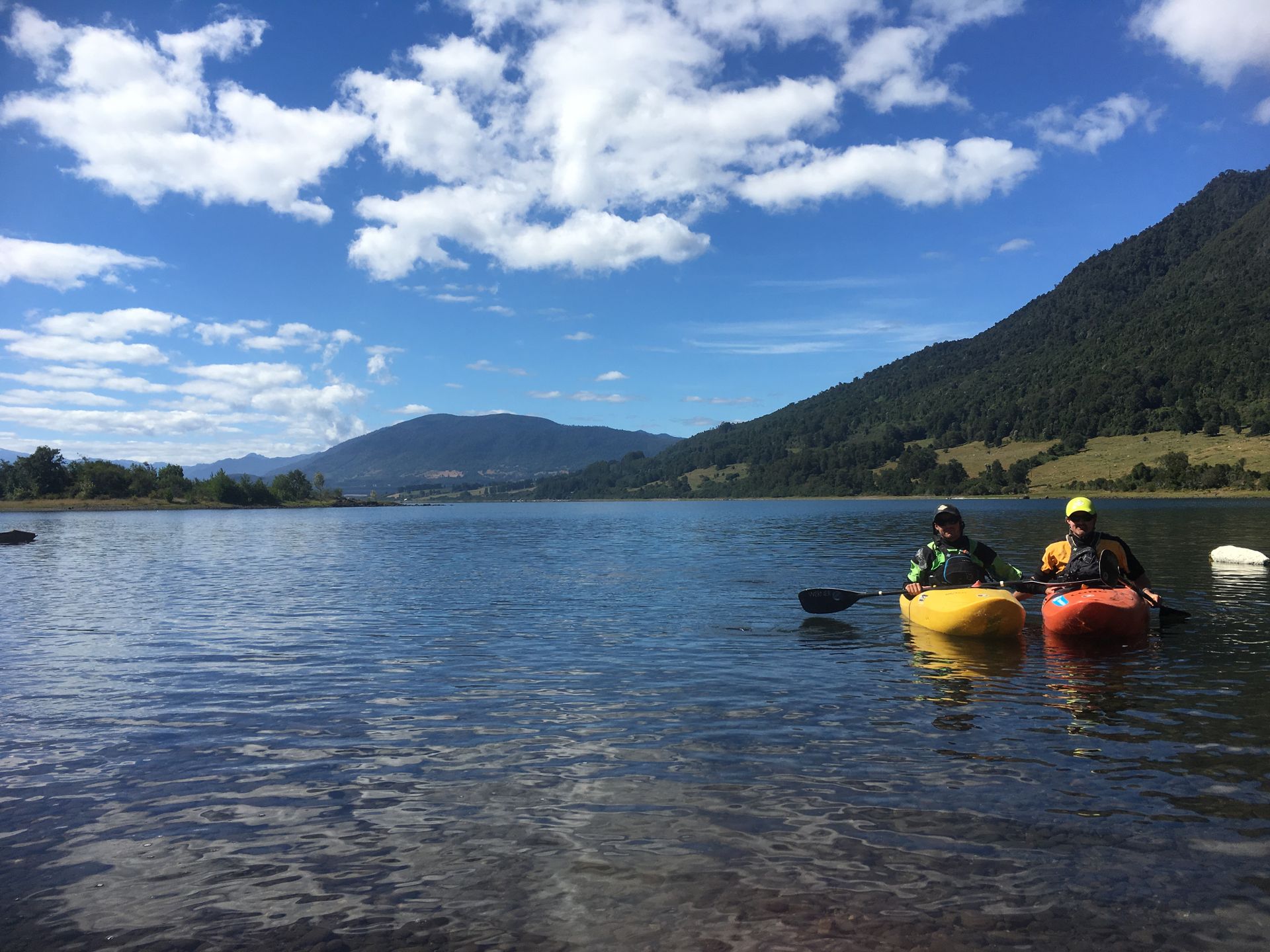 Two kayakers on a lake with mountains and forest in the background