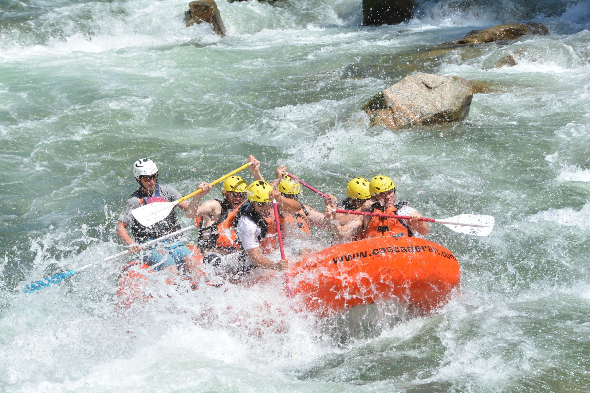 Orange raft in river paddling down rapid