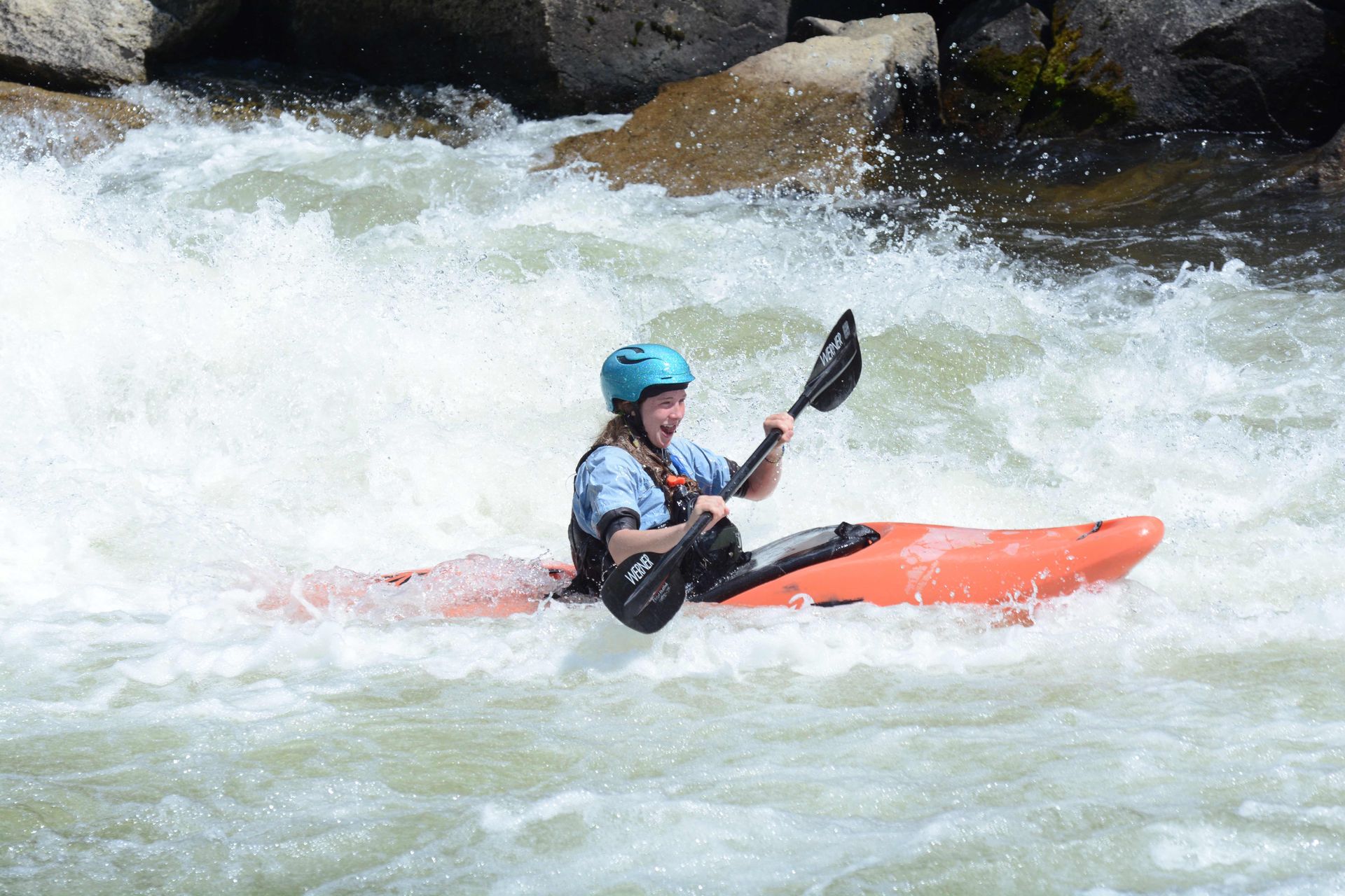 Smiling kayaker in orange boat in whitewater rapid