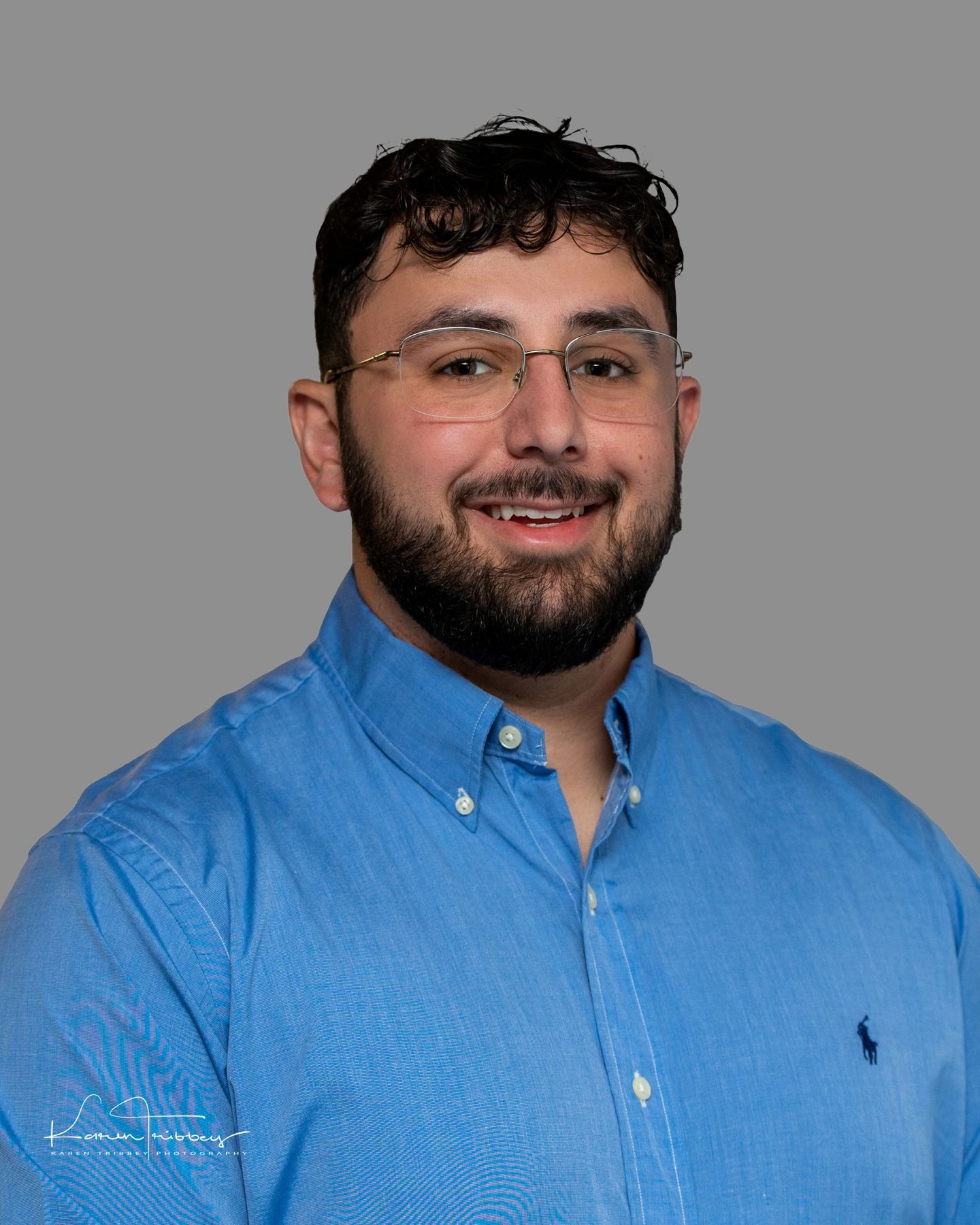 A man with a beard and glasses is wearing a blue shirt.