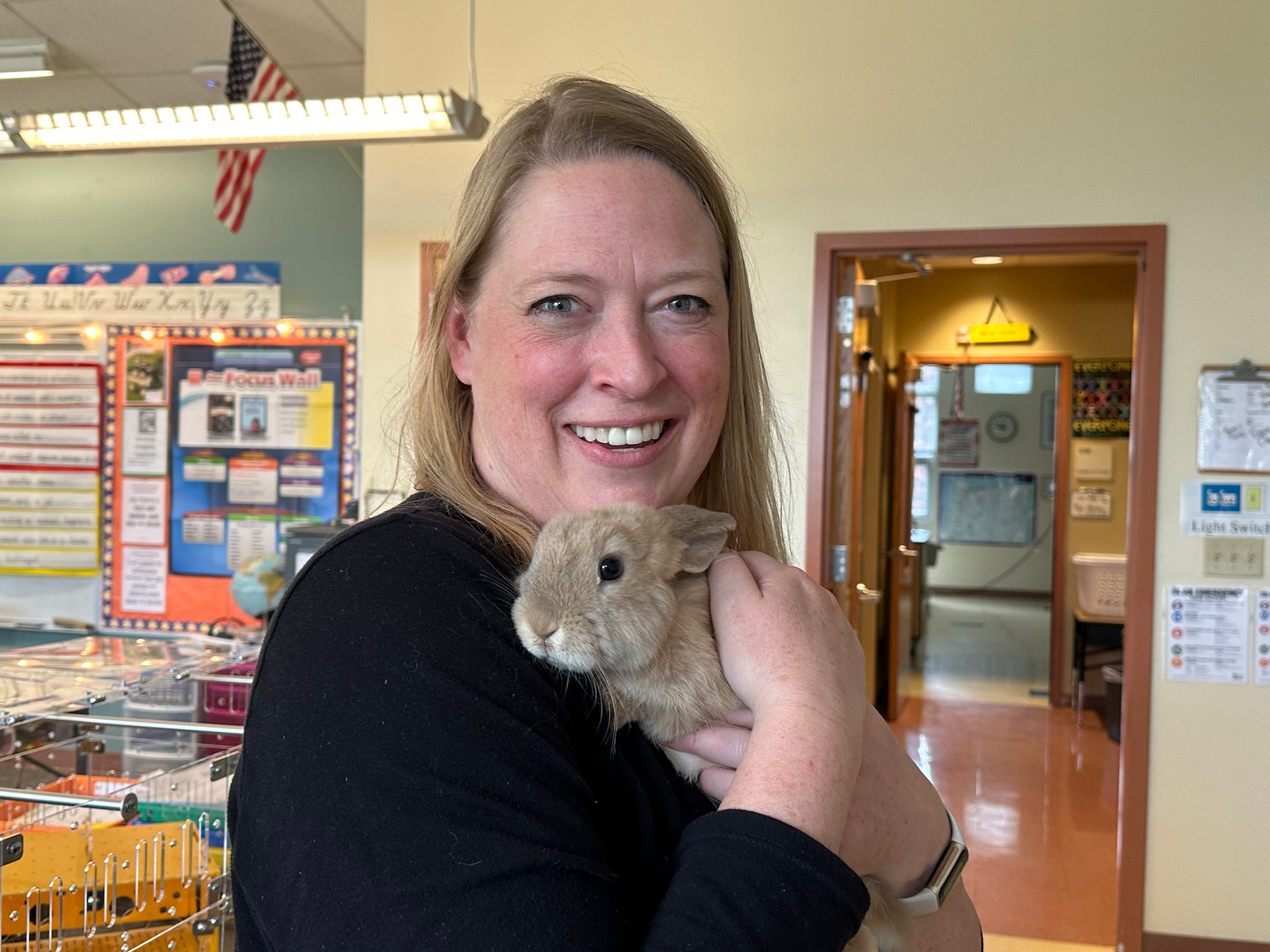 Blonde female teacher holding a small beige Netherland dwarf bunny.