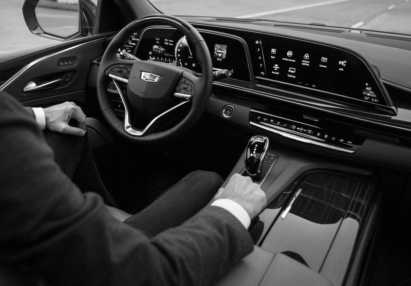 A man in a suit is driving a cadillac escalade.