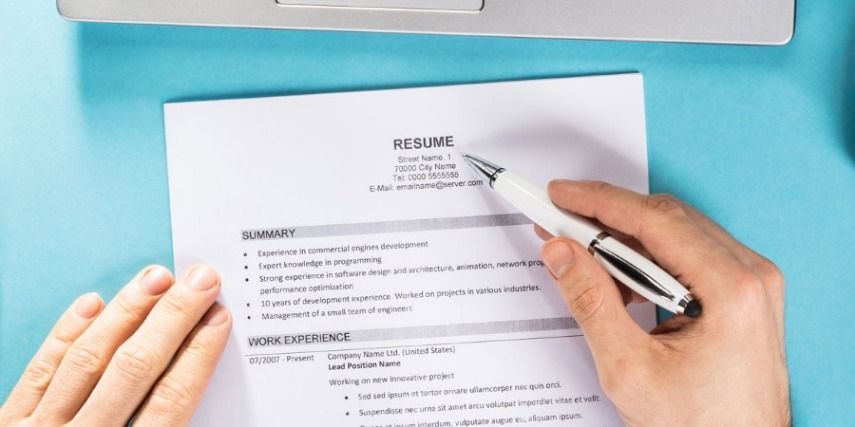 A person is writing on a resume with a pen.