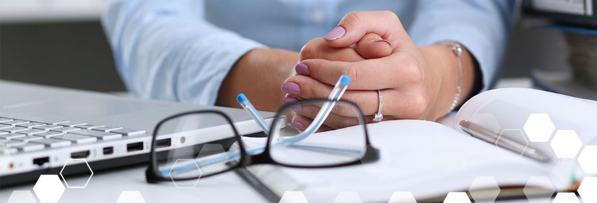 A woman is sitting at a desk with a laptop and glasses.