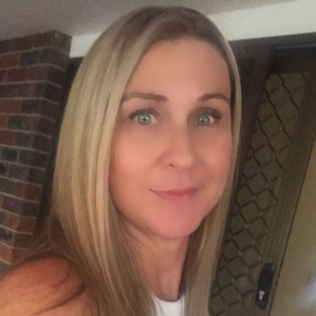 A woman with blonde hair is smiling in front of a brick wall