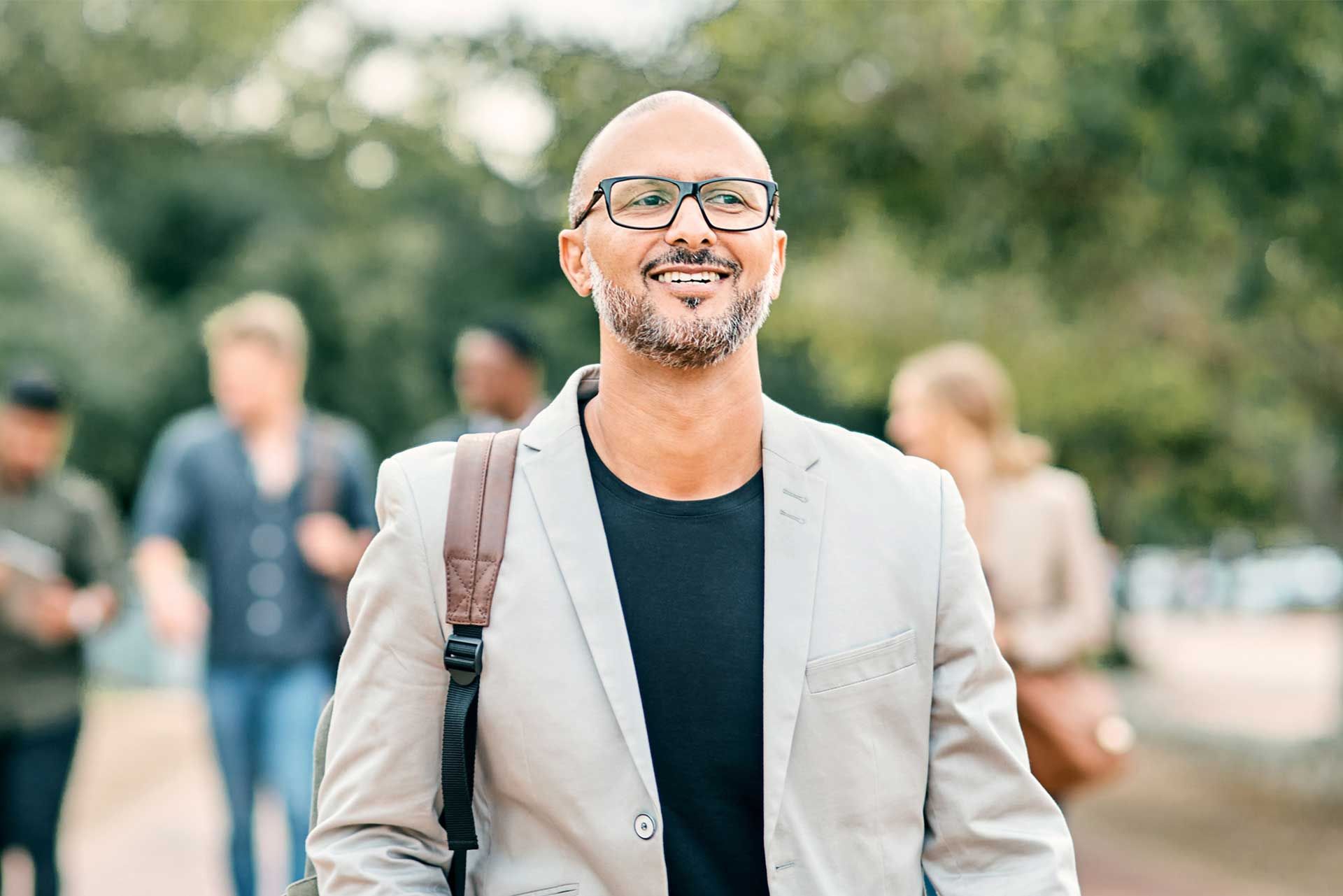 A man in a suit and glasses is smiling while walking in a park.