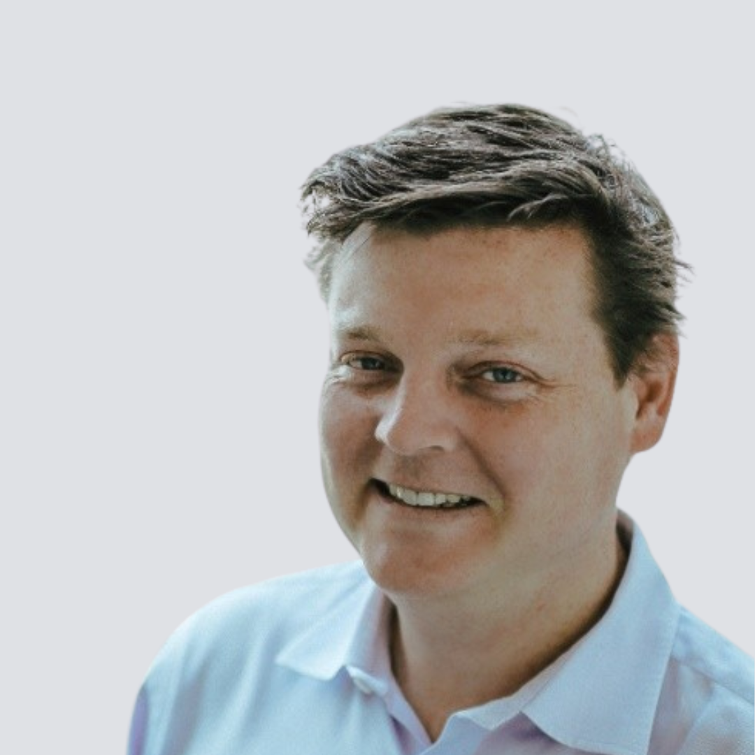 A man in a light blue shirt smiles for the camera