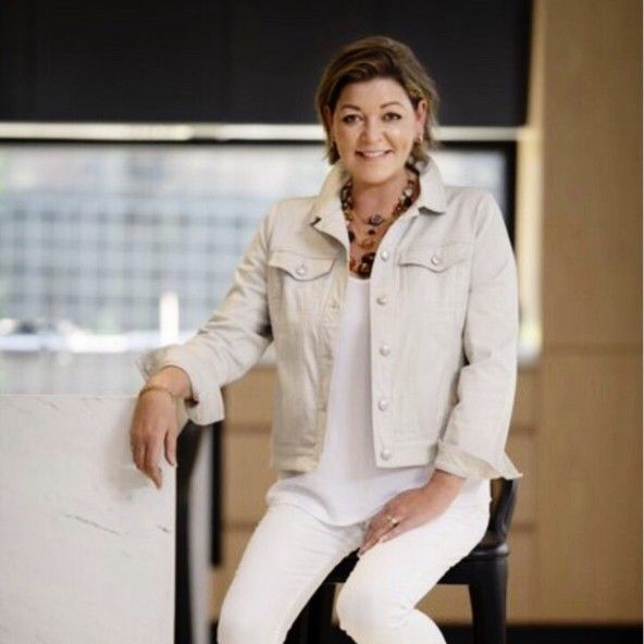 A woman in a white jacket and white pants is sitting on a stool