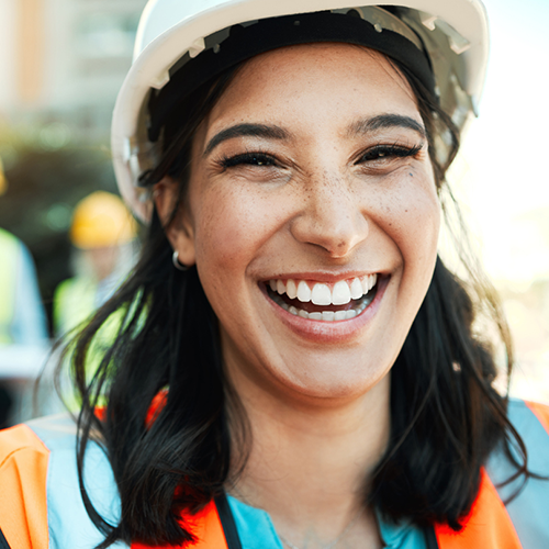 A woman wearing a hard hat and safety vest is smiling.