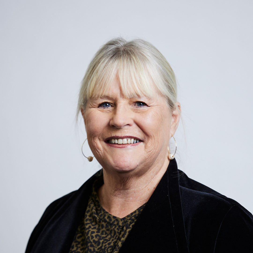 A woman wearing a black jacket and earrings is smiling for the camera.