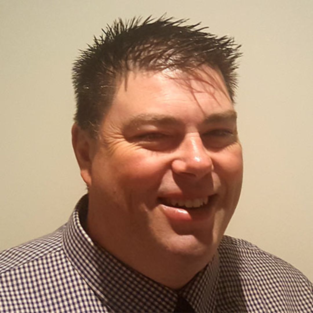 A man in a plaid shirt and tie is smiling for the camera.