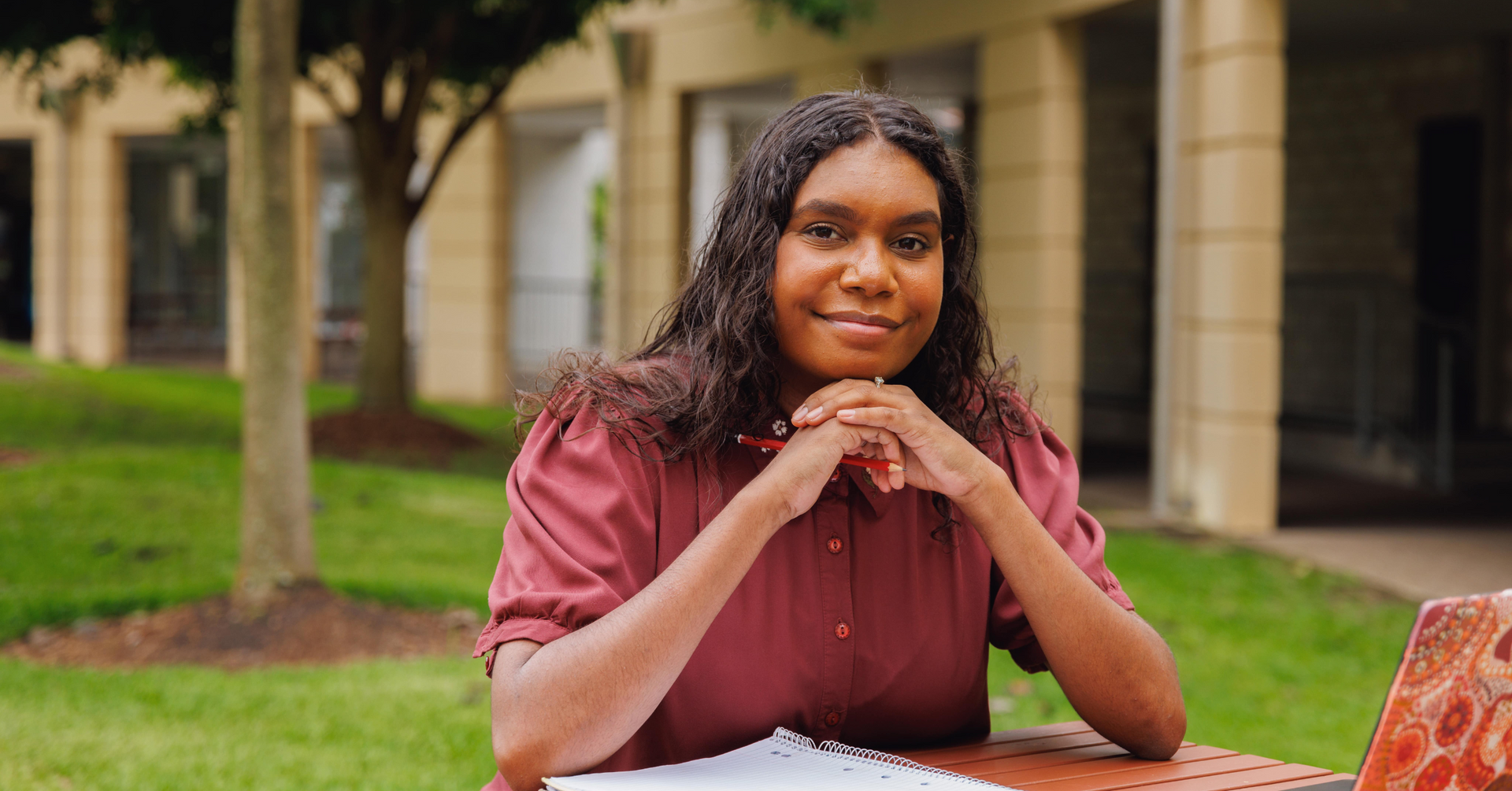 A woman is sitting at a table with her hands folded and smiling.