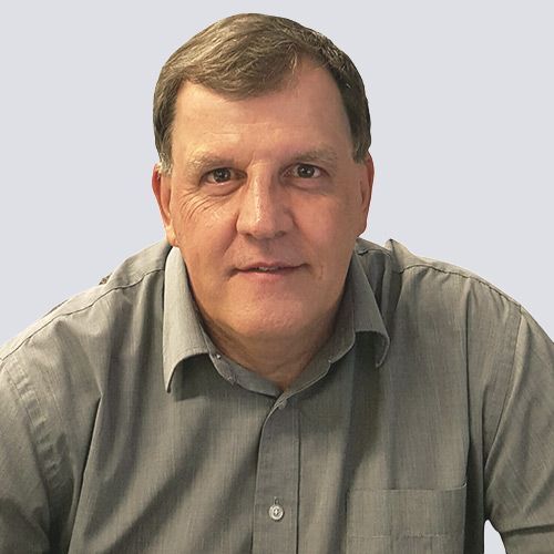 A man in a grey shirt is sitting at a table and smiling at the camera.