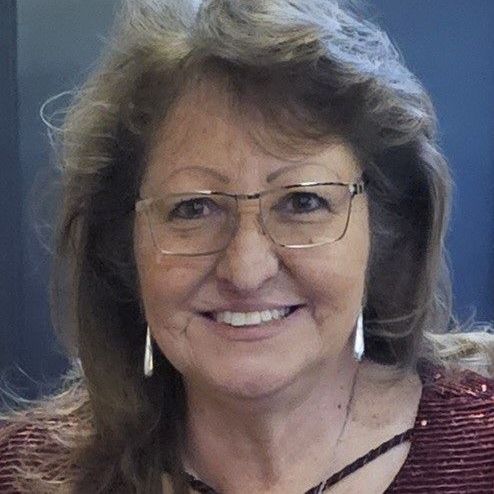 A woman wearing glasses and earrings is smiling for the camera.