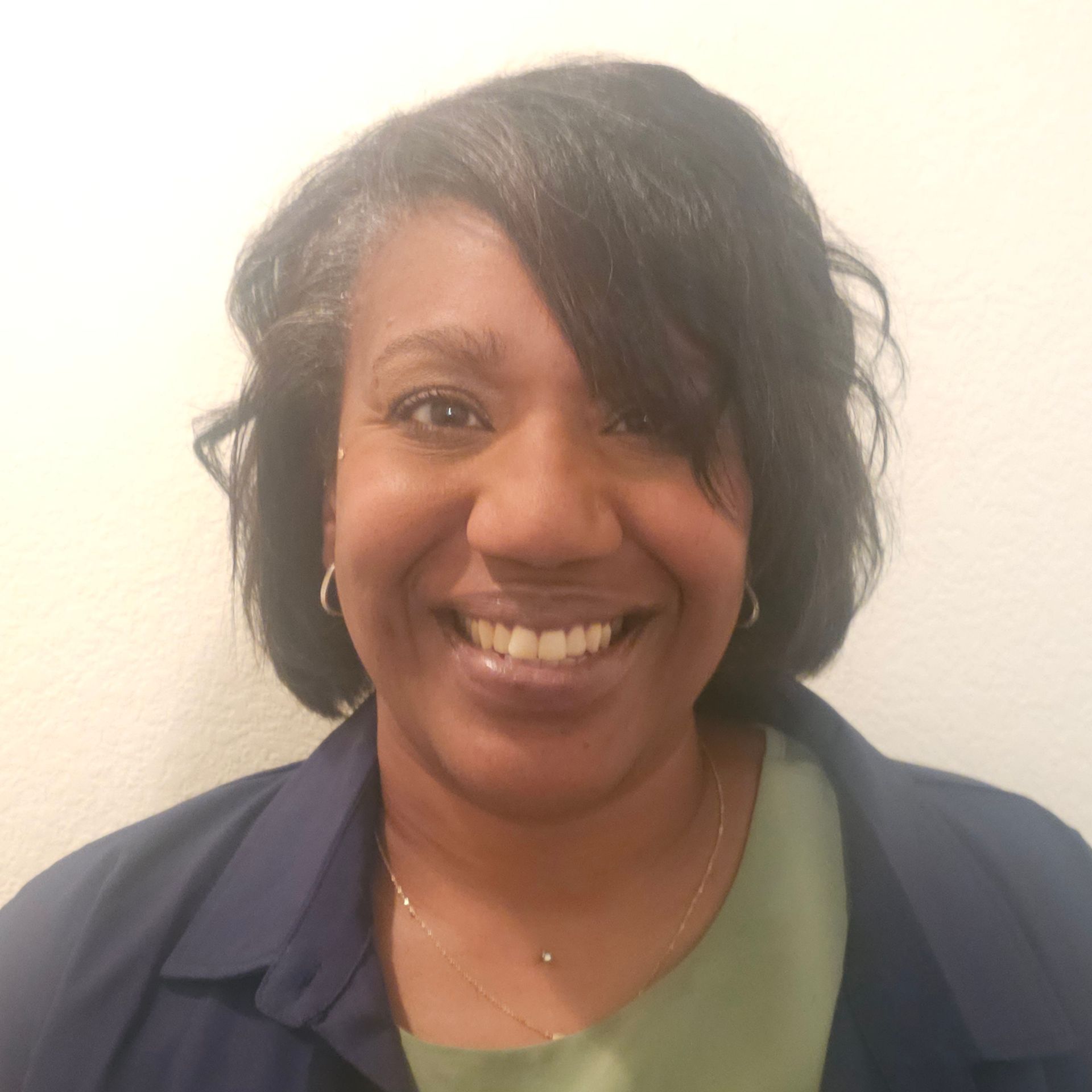 A woman in a blue jacket and green shirt is smiling for the camera.