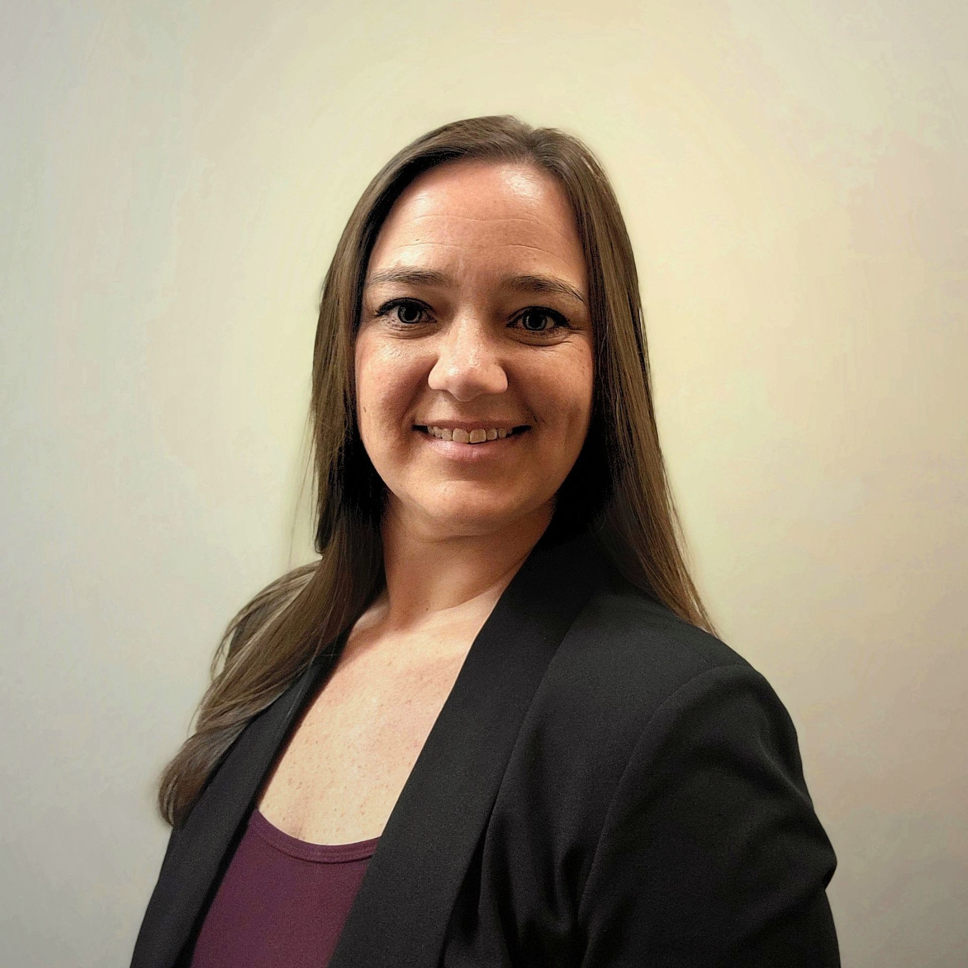 A woman wearing a black jacket and a purple shirt smiles for the camera