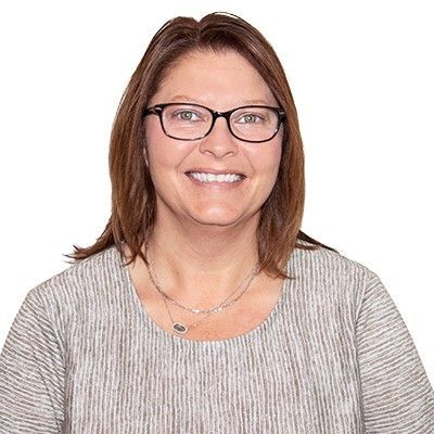 A woman wearing glasses and a necklace is smiling for the camera.