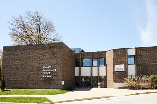 Brick office building with a central entrance, white signage, and trees on a sunny day