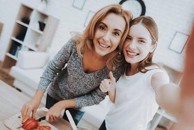 Two smiling people posing in a bright kitchen, one holding a bowl and the other holding the camera