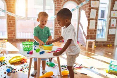 Two children playing with colorful toys at a table in a bright classroom