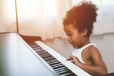 Child playing a piano keyboard indoors, looking focused in warm natural light