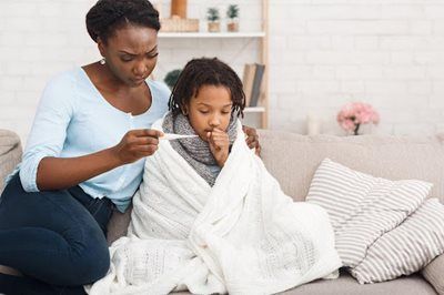 Adult comforting a child wrapped in a white blanket on a couch