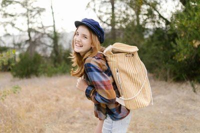 Smiling hiker in a blue hat with a tan backpack in a dry, grassy field