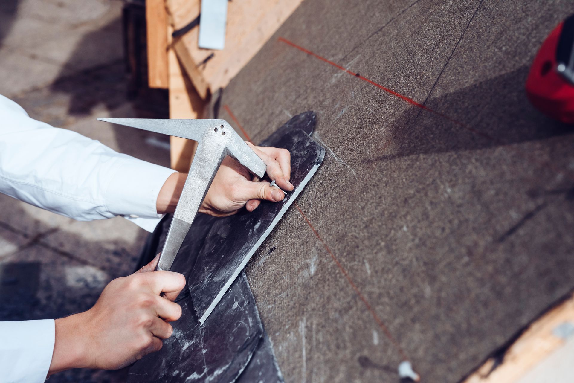 A roofer installs slate shingles with nail and hammer.