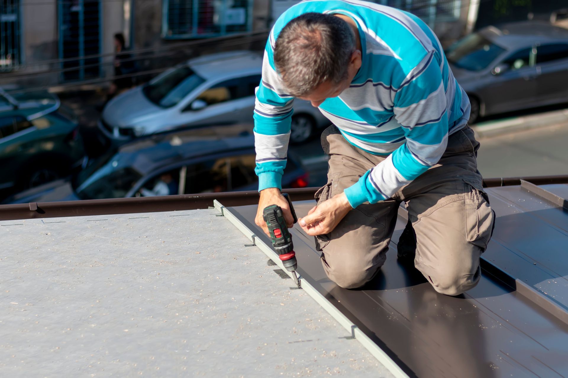 A roofer repairs and assembles sheet metal on a commercial roof with a cordless drill. A roofer repairs and assembles sheet metal on a commercial roof with a cordless drill.