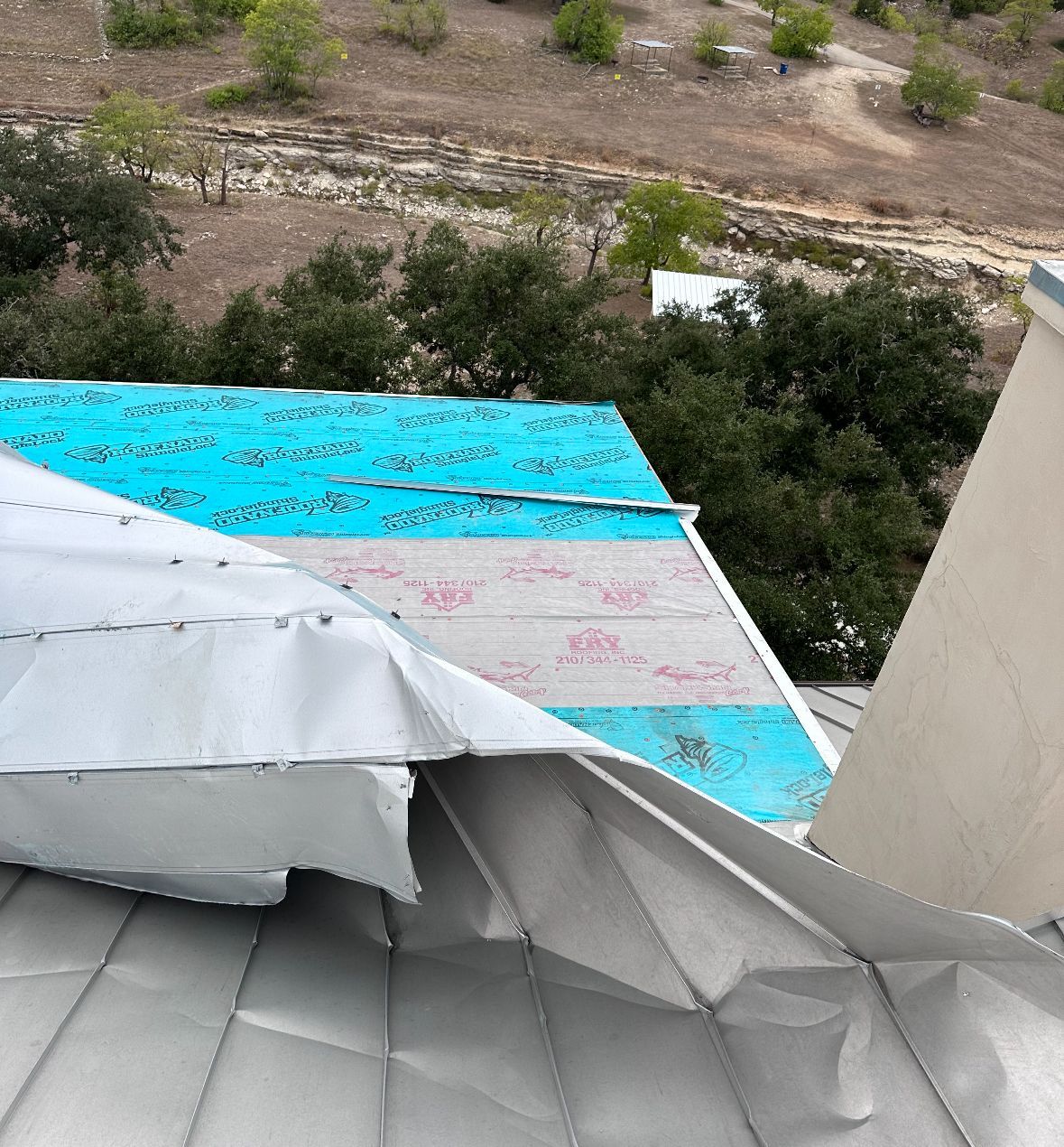 A roof with a blue tarp on it and trees in the background.