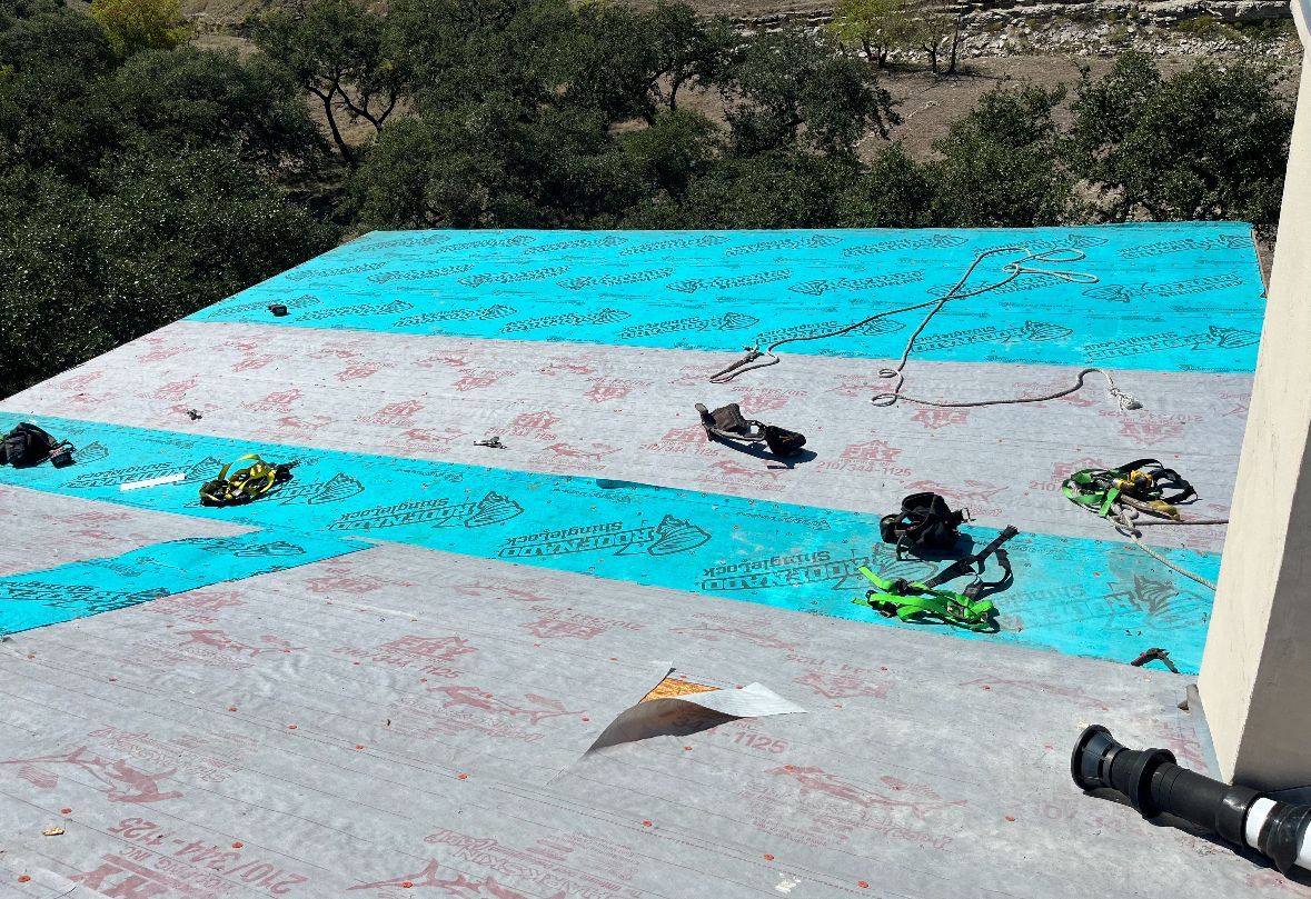 A roof with a blue tarp on it and trees in the background.
