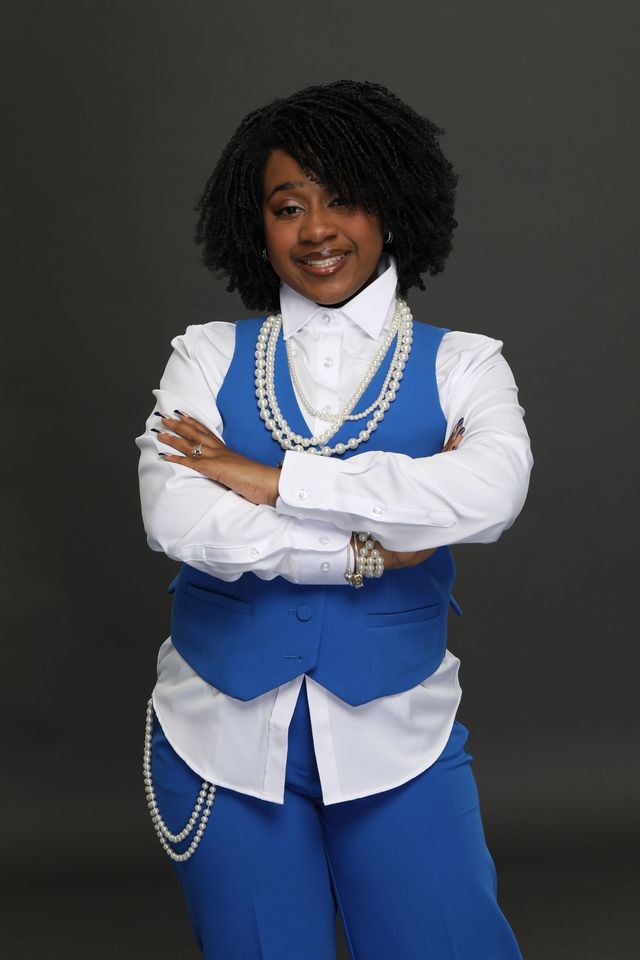 Londyn in blue-and-white layered outfit, arms crossed, smiling against a dark studio background.