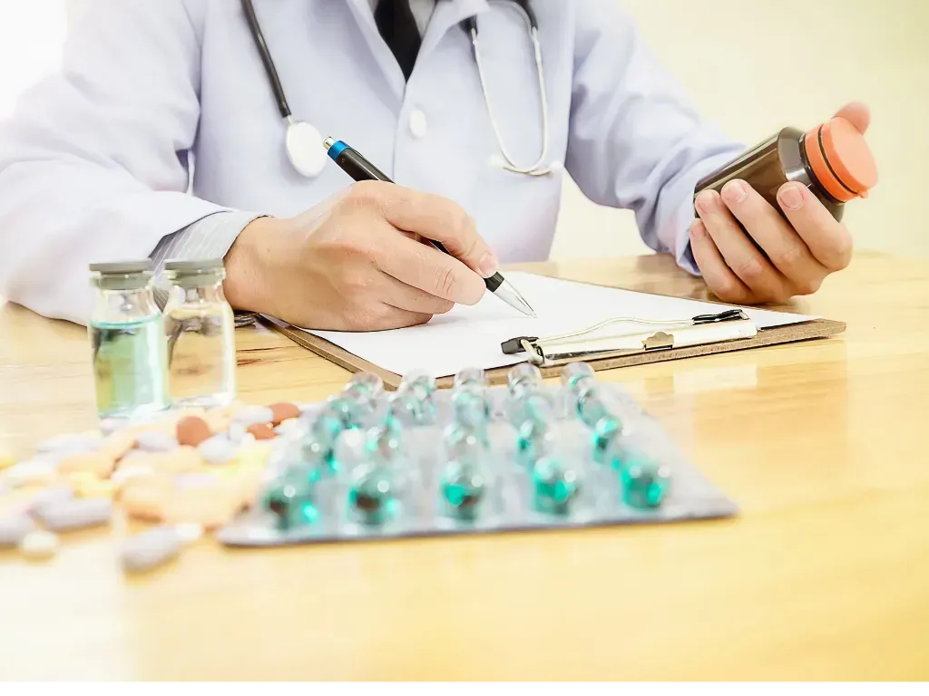 Doctor in white coat, stethoscope, writing prescription, holding pill bottle, surrounded by medications.