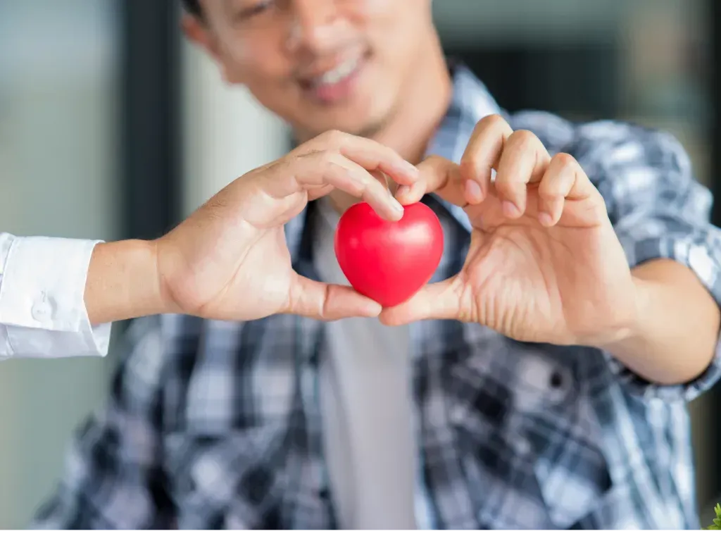 Man holding a red heart with his hands, smiling.