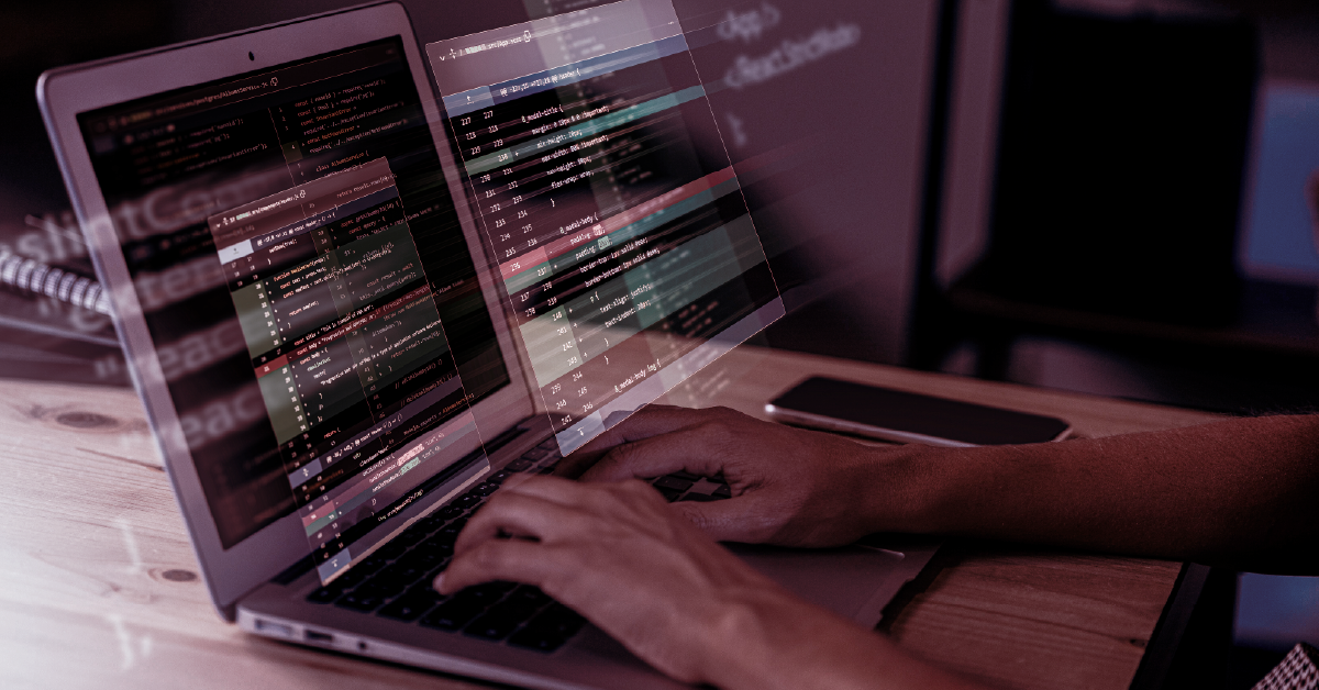 Mãos digitando em notebook com códigos de programação flutuantes sobre a tela.