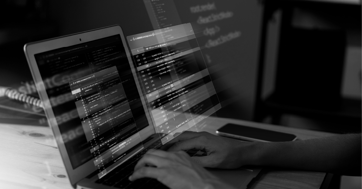 Pessoa digitando em um laptop com códigos exibidos na tela. Imagem em preto e branco.