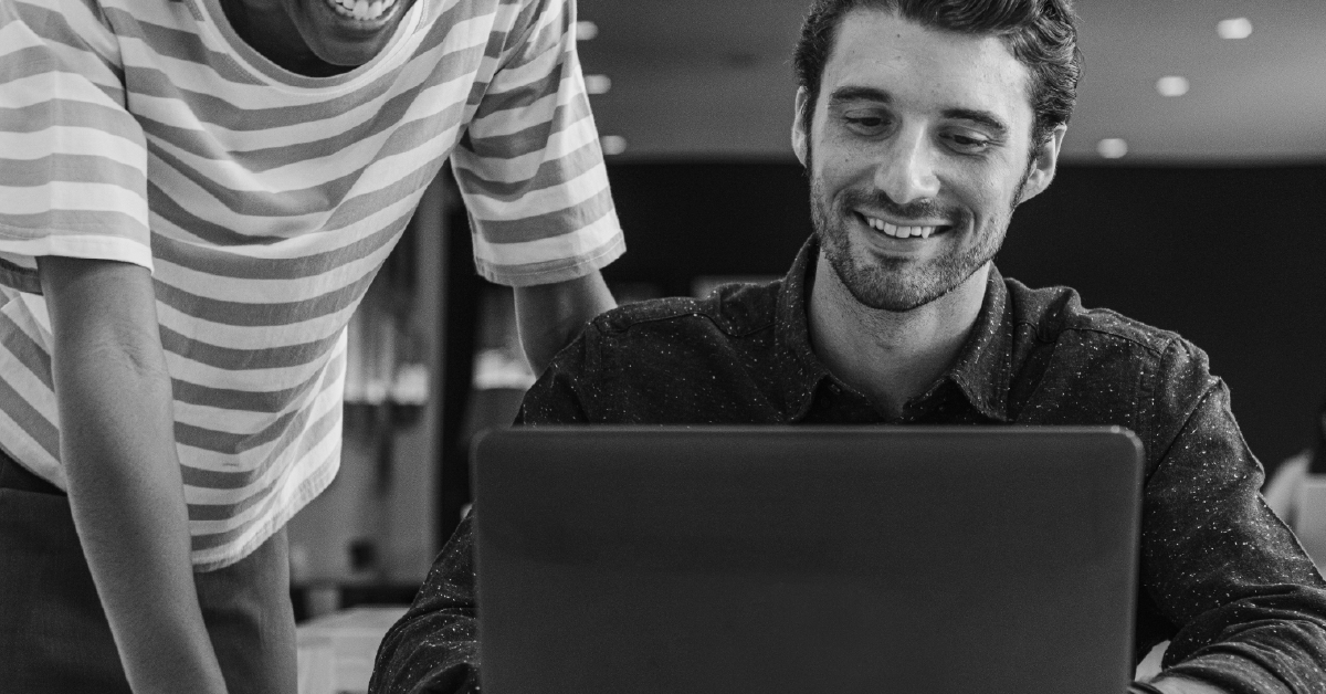 Imagem de um homem sorrindo em frente de um laptop. Imagem em preto e branco.